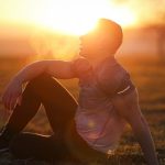 Muscular man sits in rural field at sunset, exhaling visible breath.
